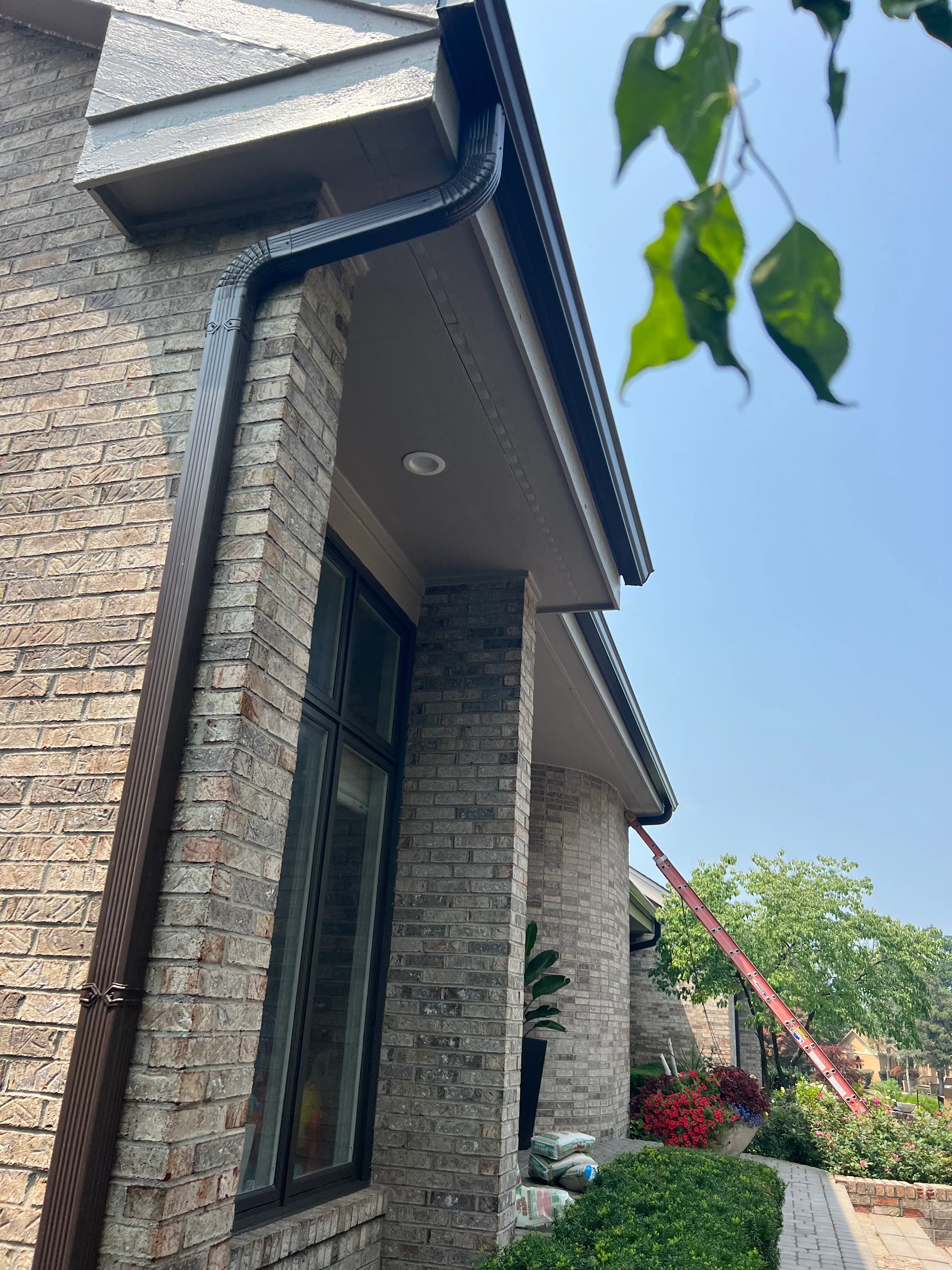 Black seamless gutter and downspout on brick home exterior with soffit