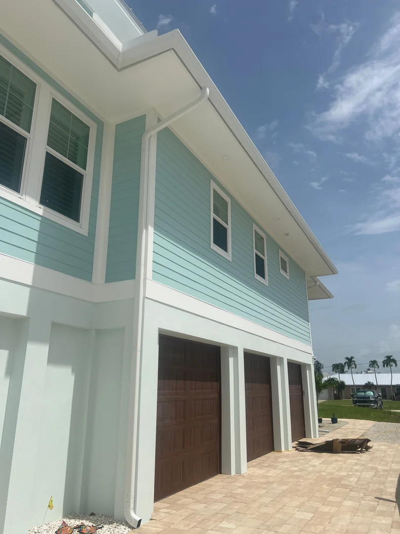 Three-story home with mint green and white horizontal siding, white trim, and dark garage doors