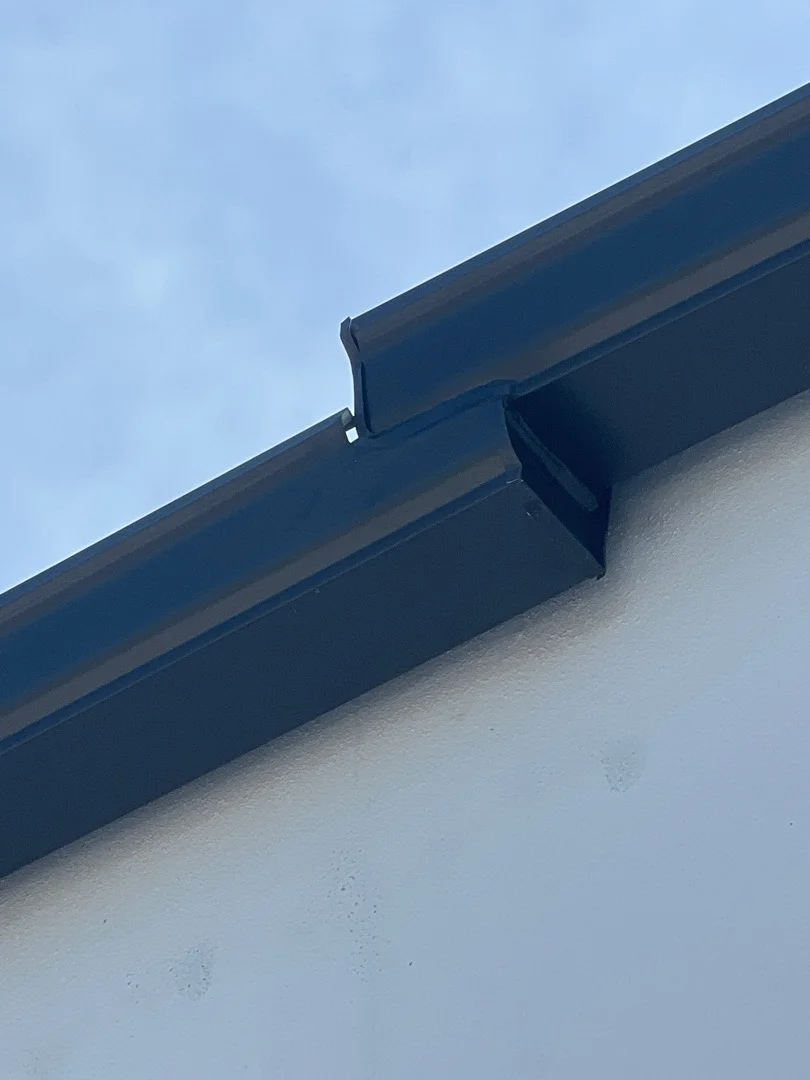 Dark blue seamless aluminum gutter with downspout installed on white fascia board