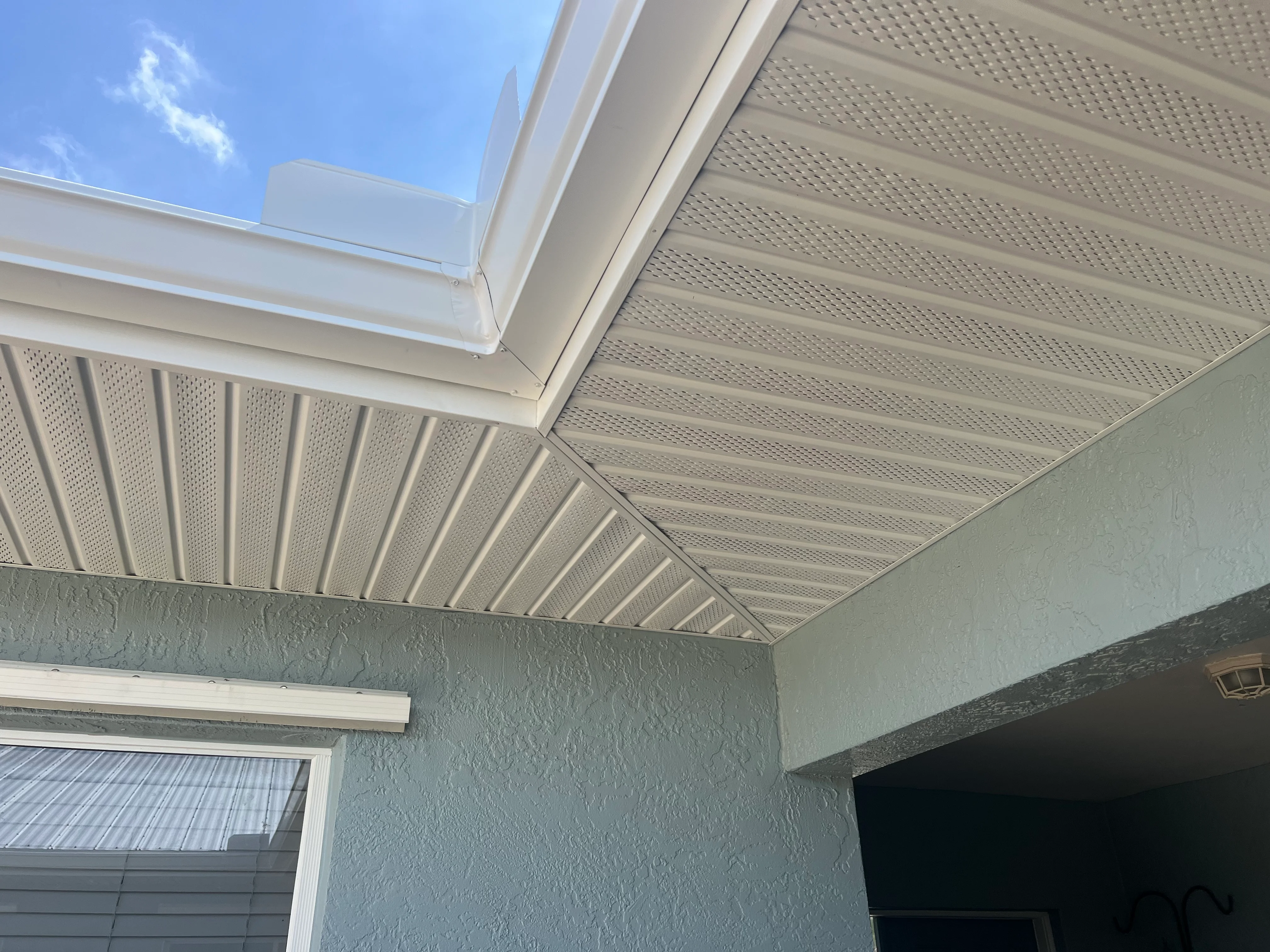 White aluminum patio cover with perforated panels and skylight above stucco wall