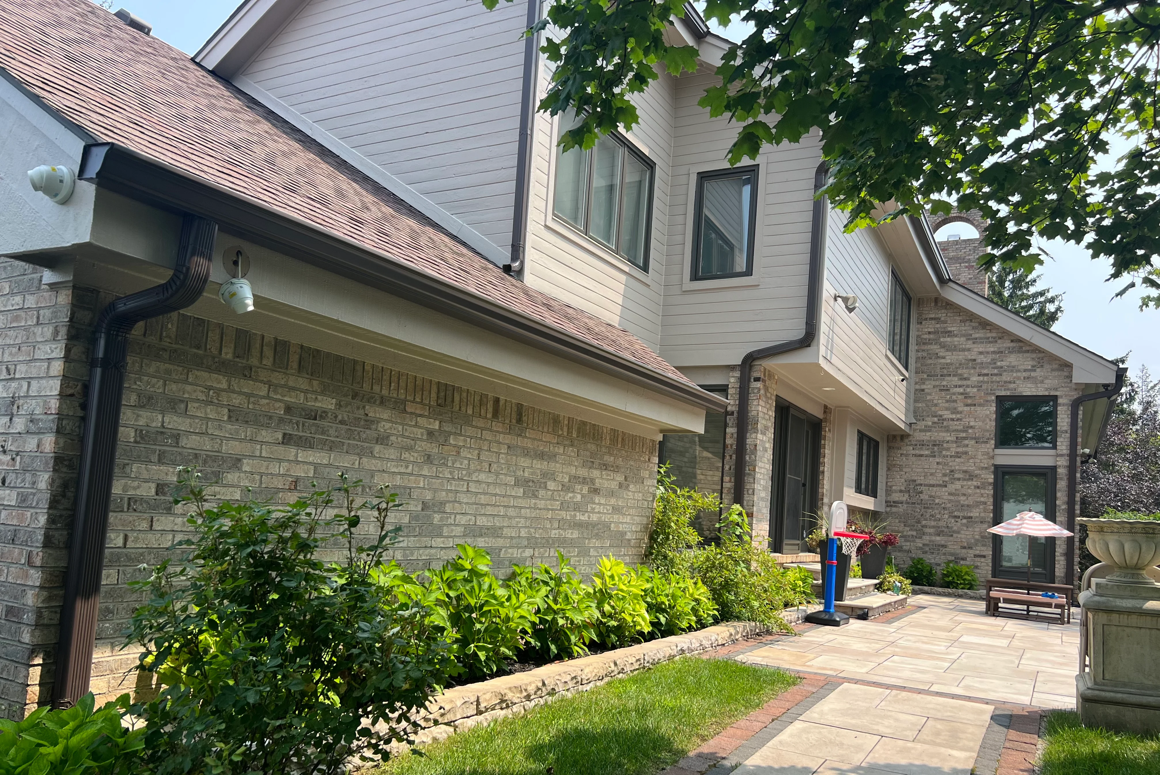 Black seamless gutters and downspout system installed on brick and siding home exterior
