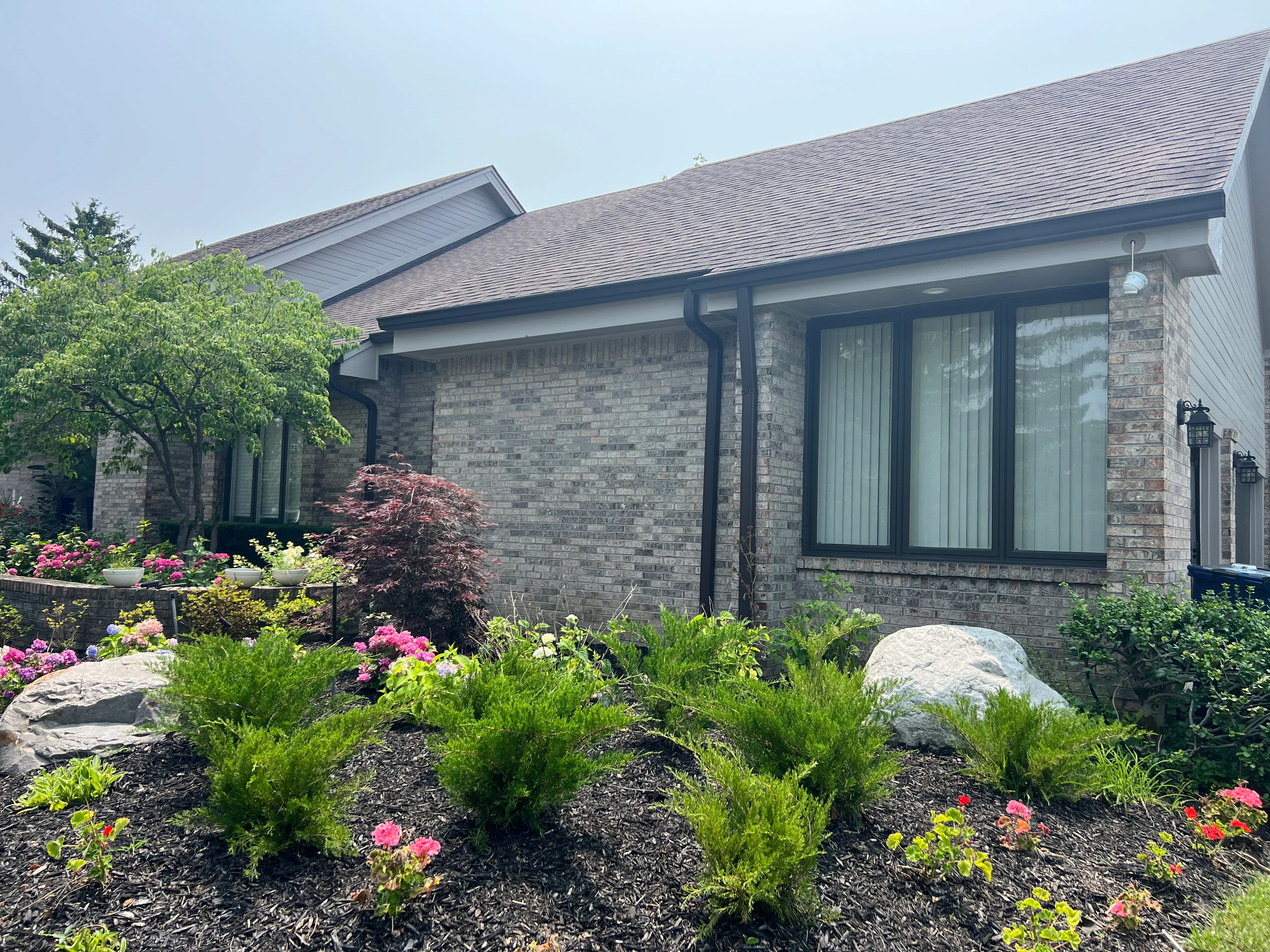 Black seamless gutters and downspouts on brick home with stone fascia and large windows