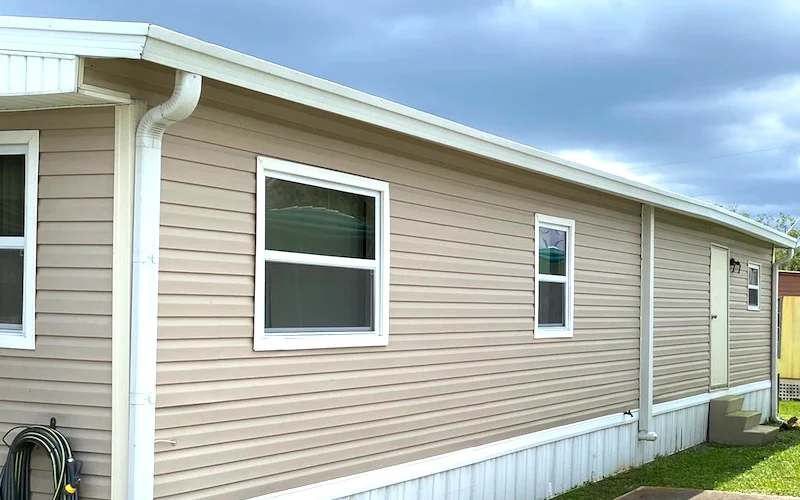 White aluminum gutters and downspouts installed on tan vinyl-sided mobile home