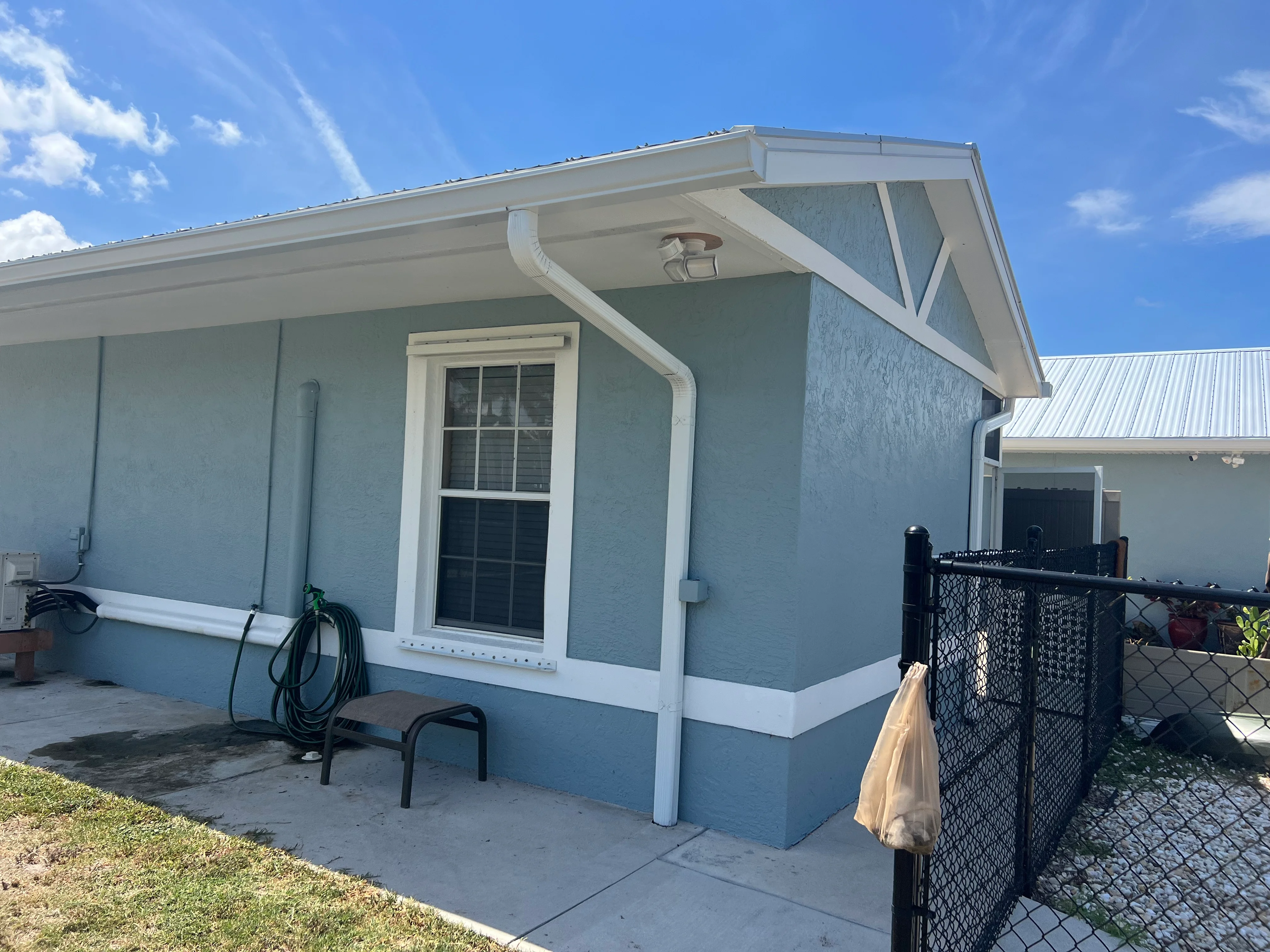 Light blue house with white trim, fascia, and gable braces against clear sky