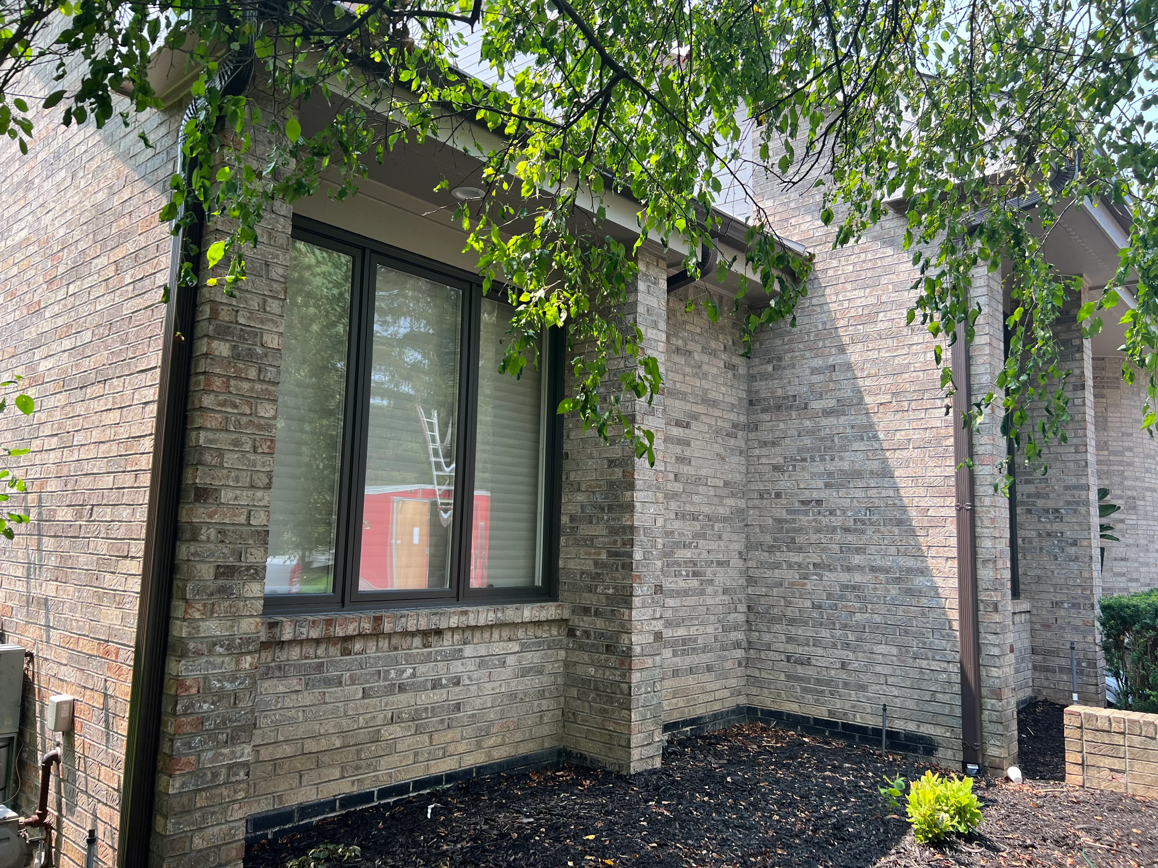 Black aluminum gutter and downspout installed on brick home exterior