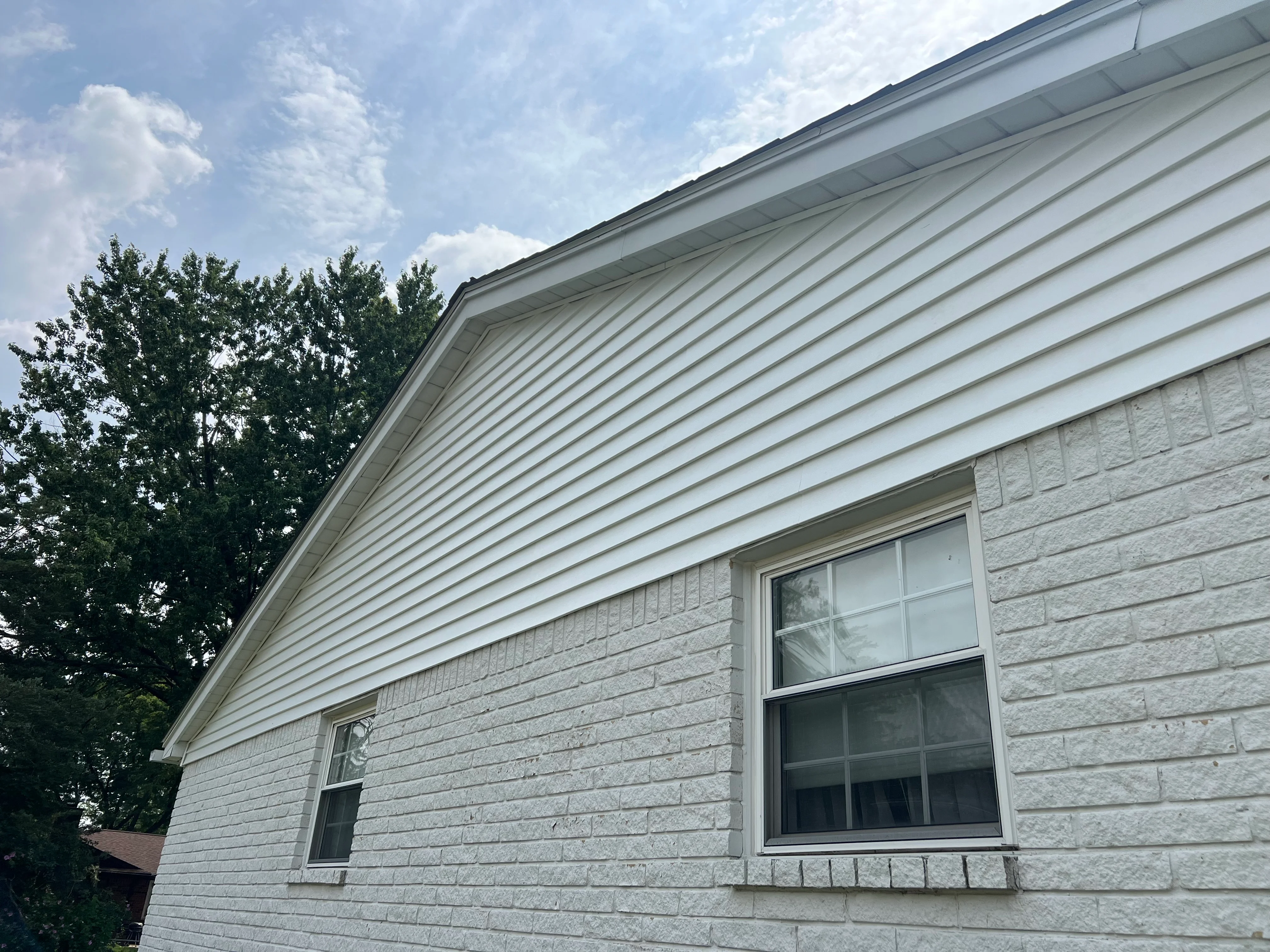 White vinyl siding with new gutters, fascia, and replacement windows on residential home