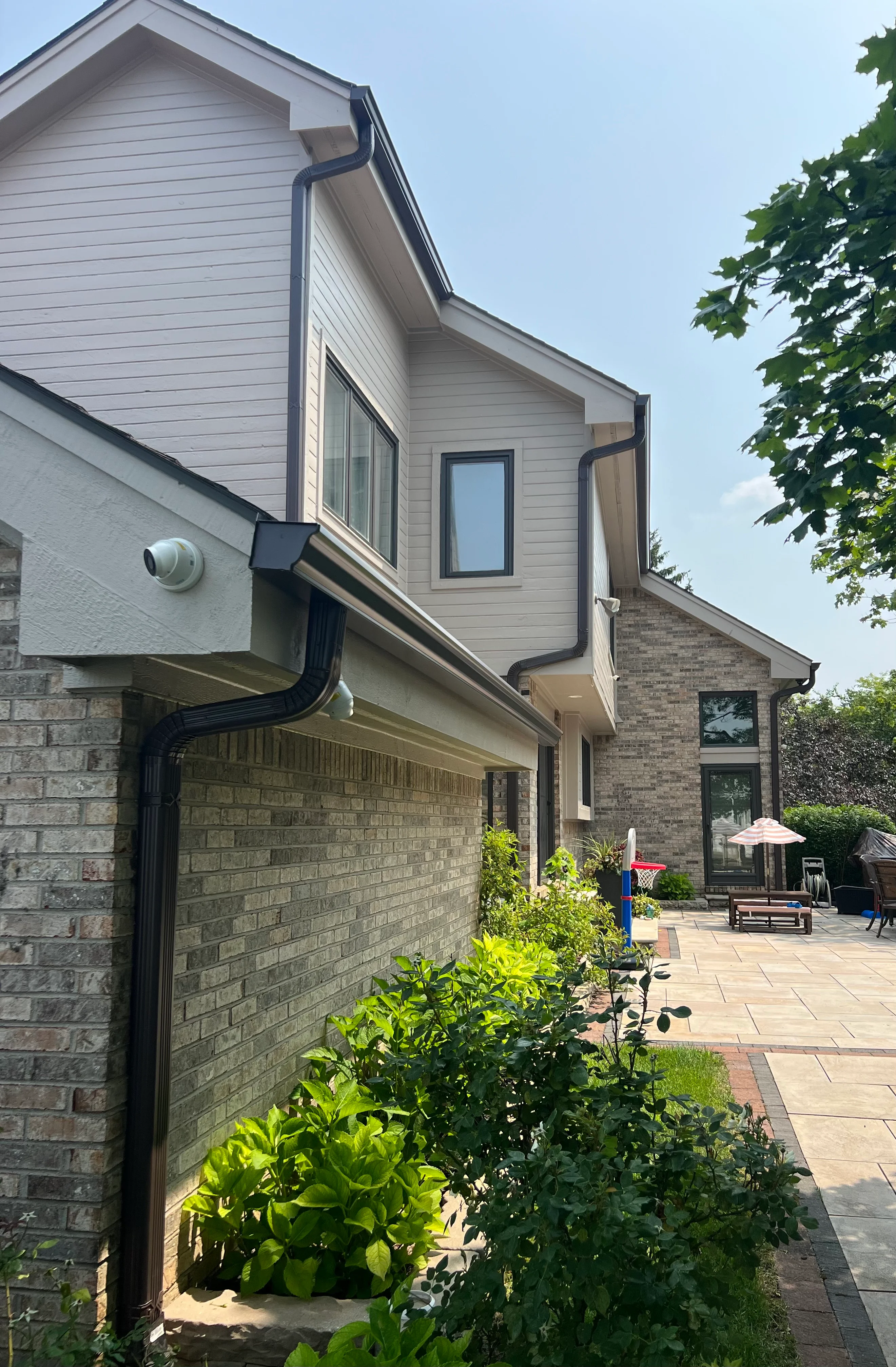 Black seamless gutters and downspout extensions on two-story brick and siding home
