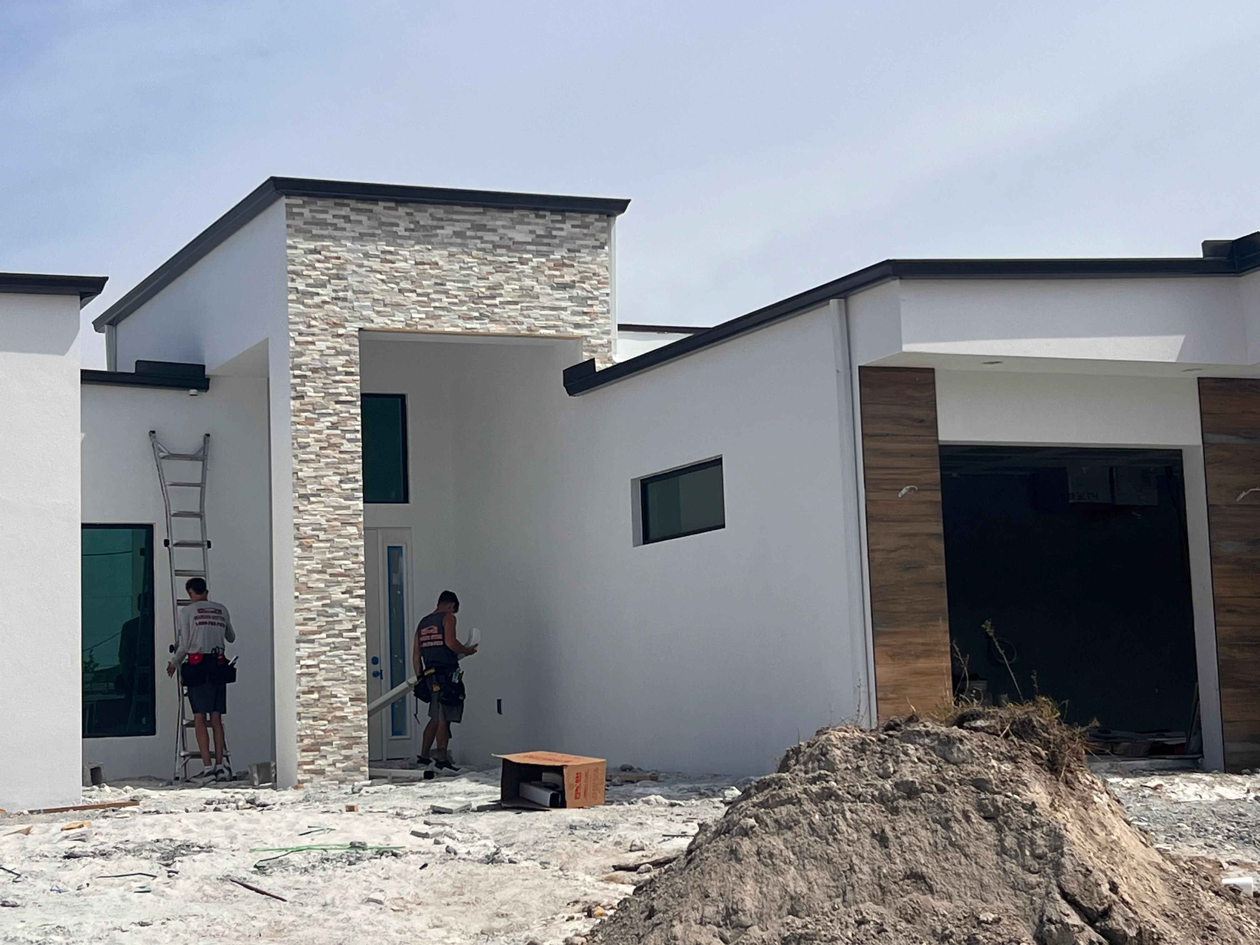 Modern home with white stucco walls, stone veneer chimney accent, and black metal trim during construction phase