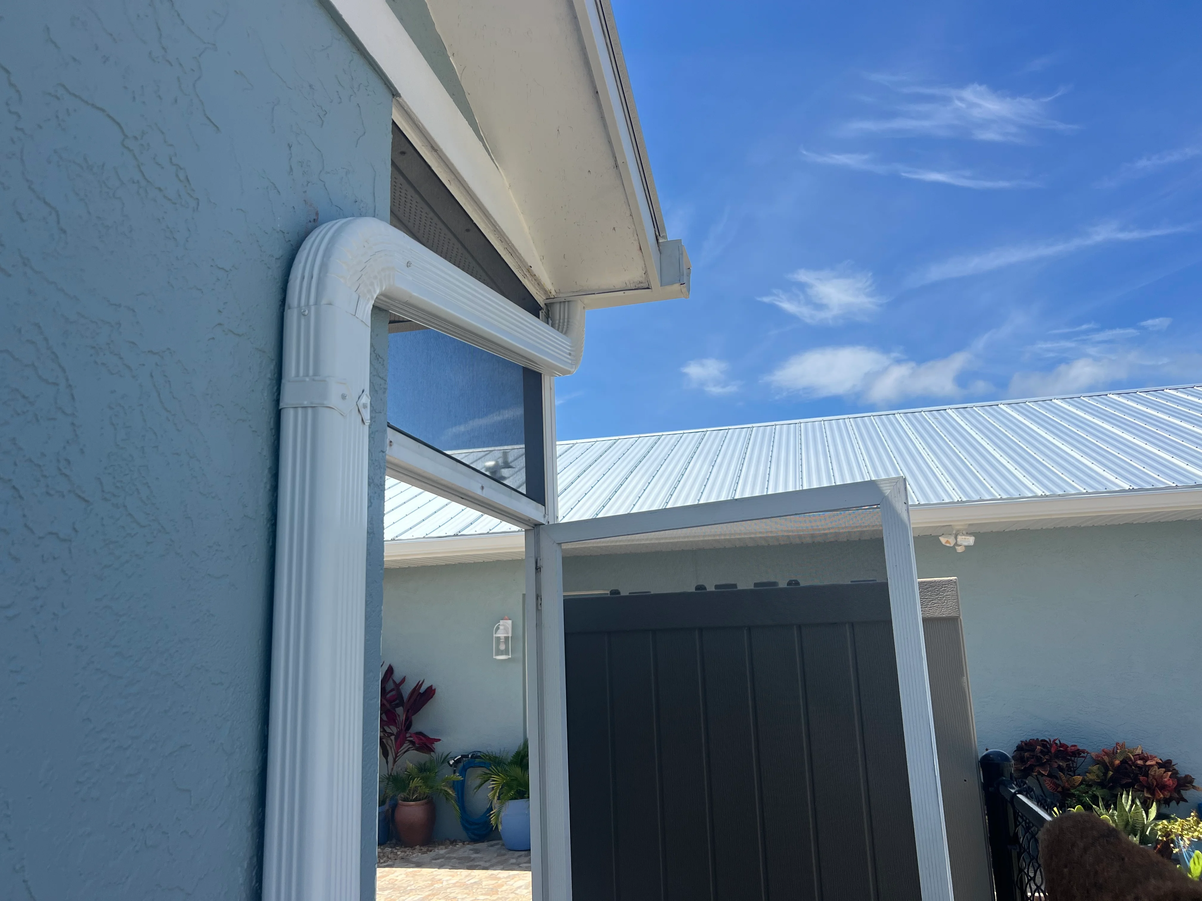 White aluminum gutters and downspouts installed on residential home with metal roof